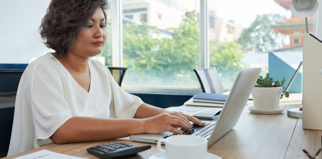 mulher-com-cabelo-ondulado-curto-sentado-na-mesa-no-escritorio-e-trabalhando-no-laptop