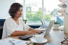 mulher-com-cabelo-ondulado-curto-sentado-na-mesa-no-escritorio-e-trabalhando-no-laptop